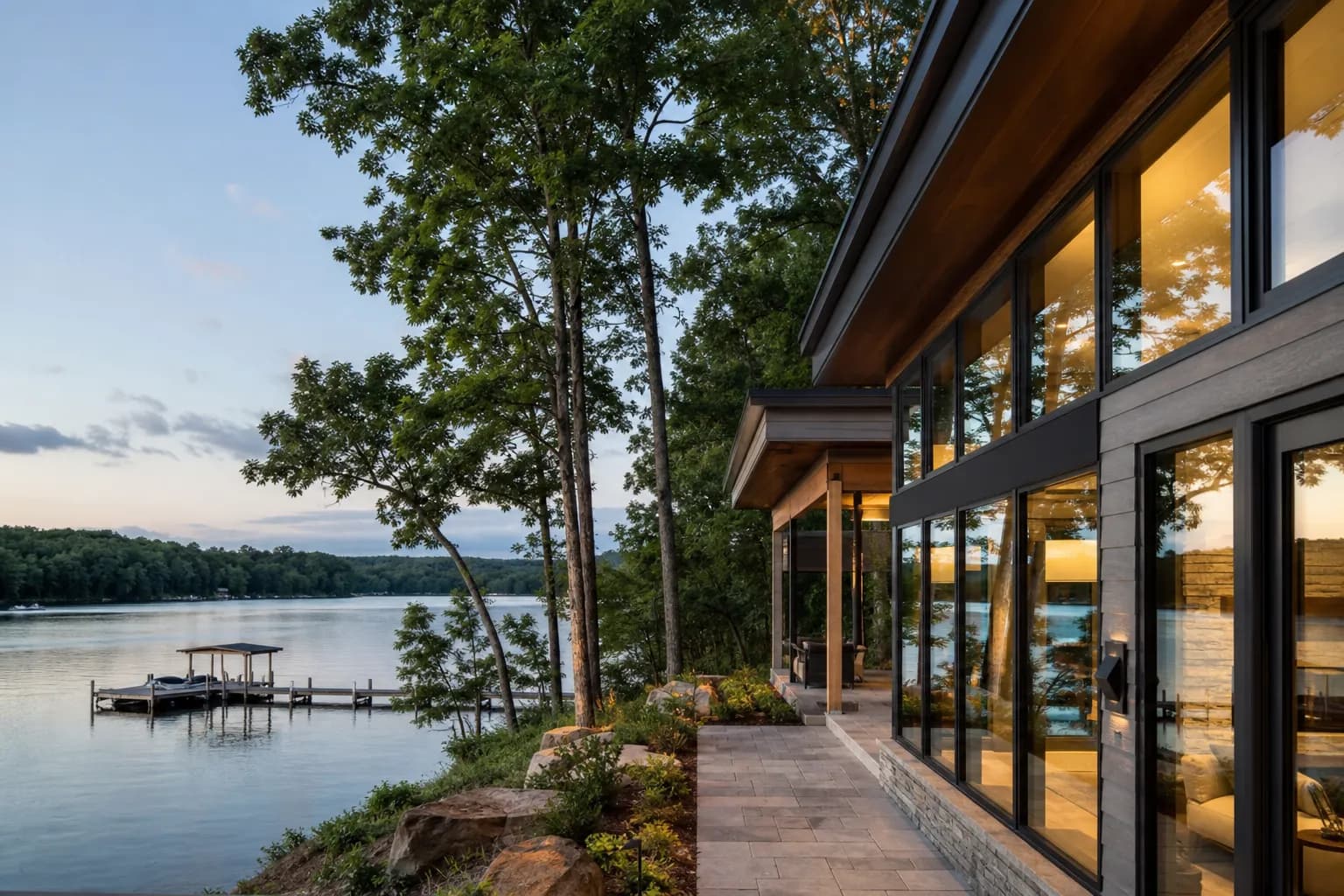 Lake house with walls of new windows facing a wide reservoir with a boat dock.